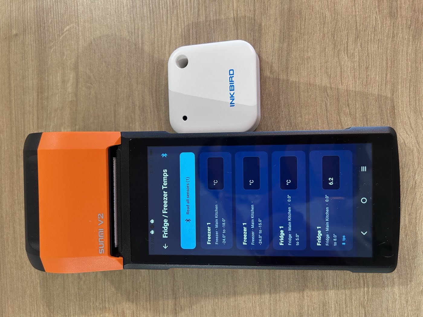 Fridge and freezer temperature screen on the Sunmi V2 handheld beside an Inkbird Bluetooth temperature sensor