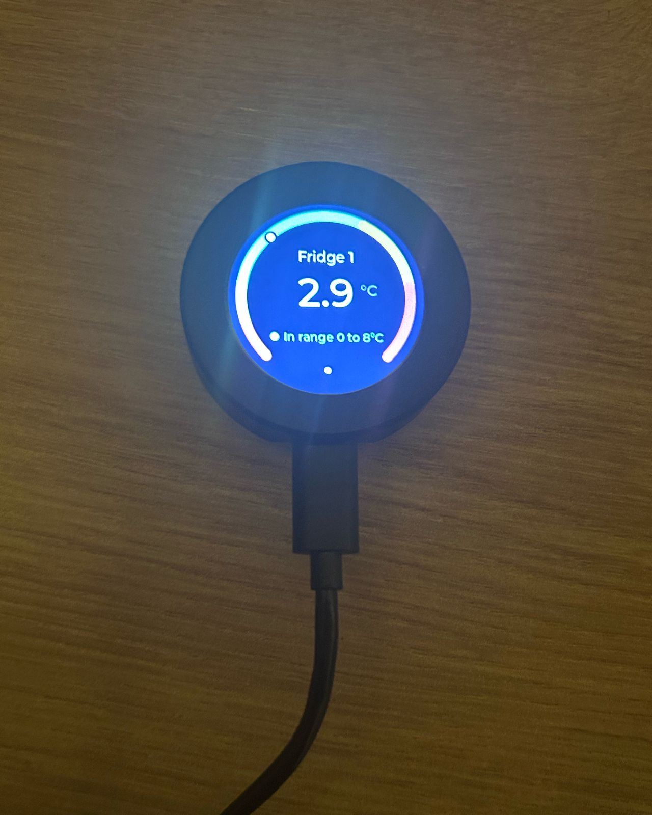 A CompliChef Round on a wooden worktop, plugged into USB-C power, showing Fridge 1 at 2.9°C, in range 0 to 8°C